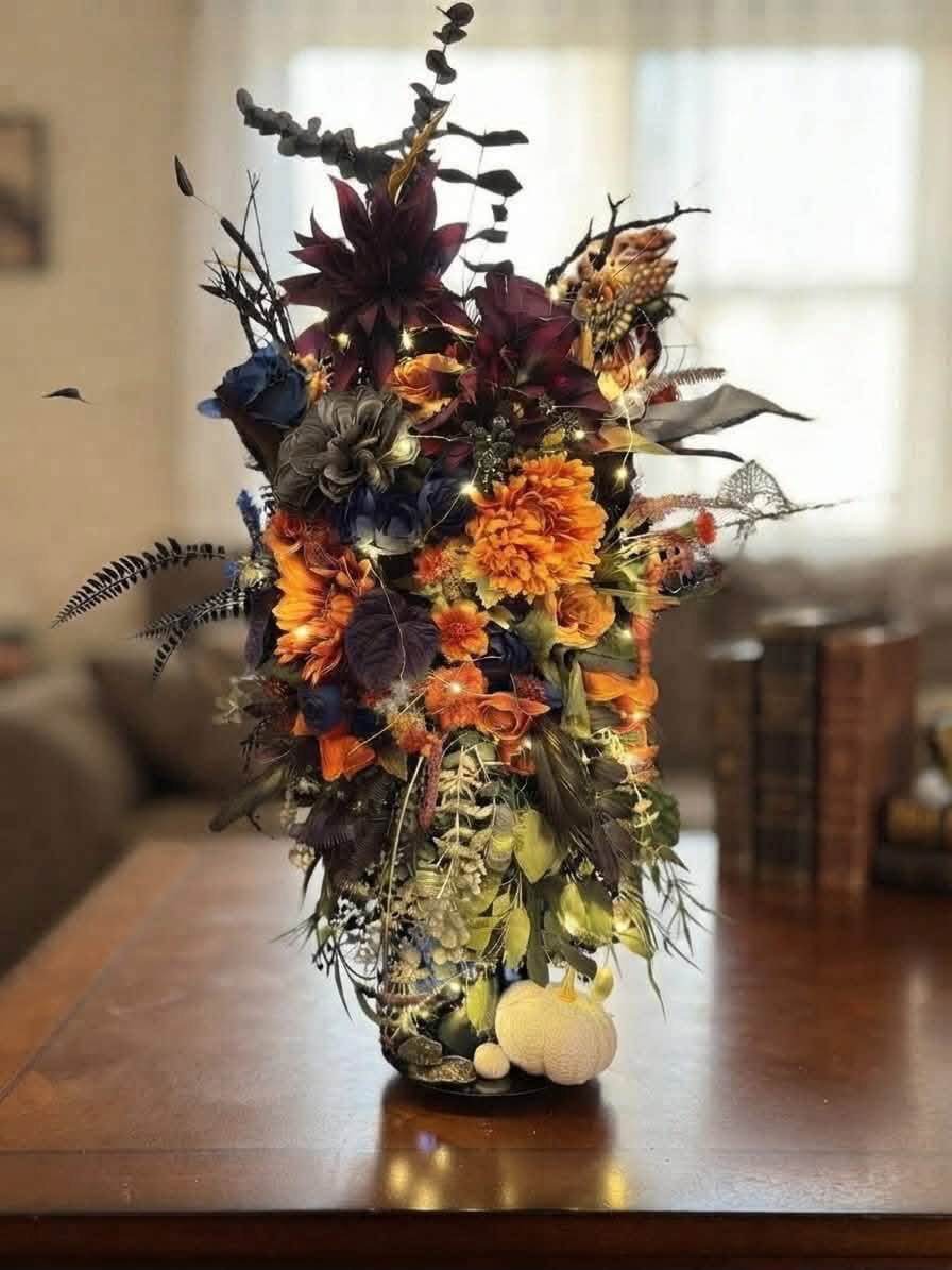Tall vase filled with orange, burgundy and navy artificial flowers and trailing decorative greenery