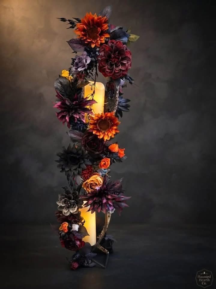 Tall decorative arrangement of burgundy and orange artificial flowers around glowing pillar lights