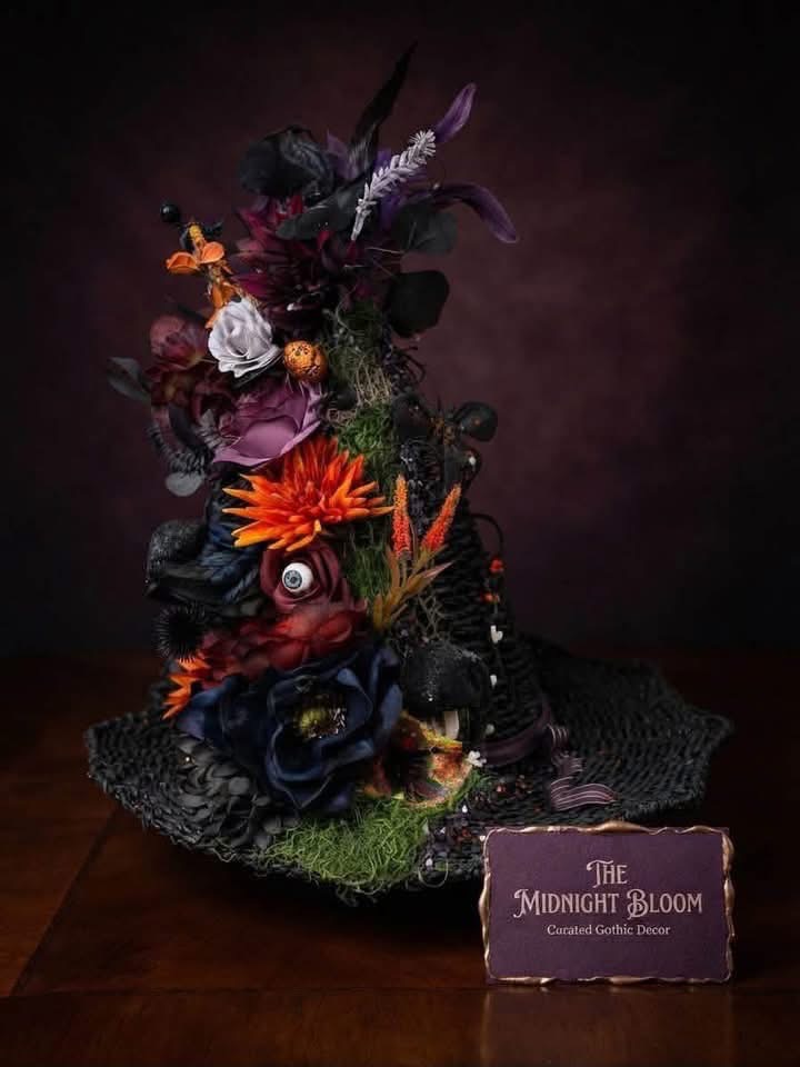 Decorative witch hat with burgundy, orange and black artificial flowers and Halloween accents